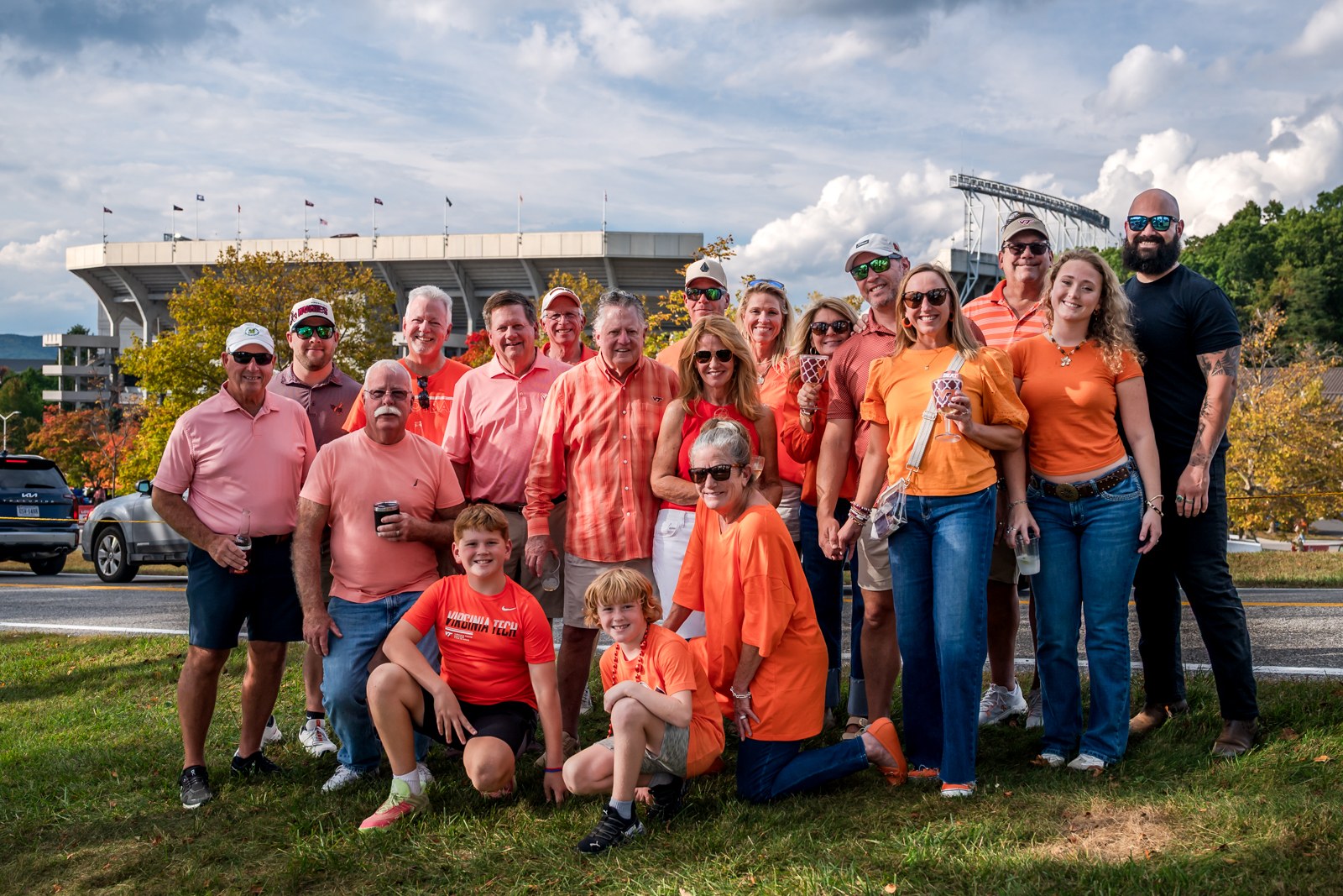 Virginia Tech tailgate group with adults and children in orange and maroon, with the stadium behind them.