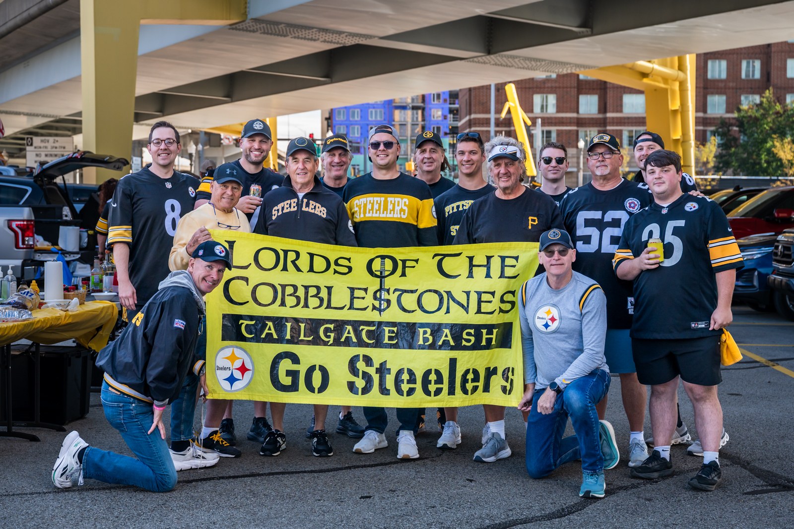 Steelers supporters holding a yellow Lords of the Cobblestones tailgate banner.