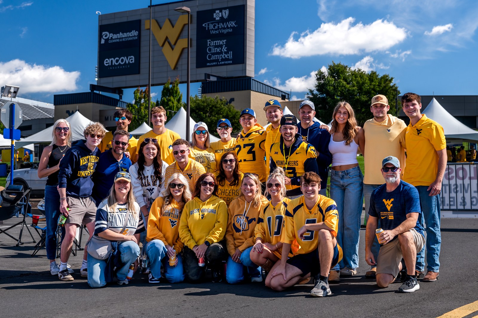 WVU fans in yellow and blue posing together beneath a WVU sign.