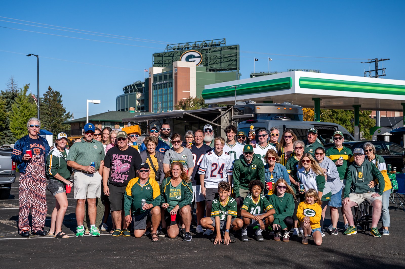 Large group of Packers and Bears fans gathered beside an RV with Lambeau Field behind them.