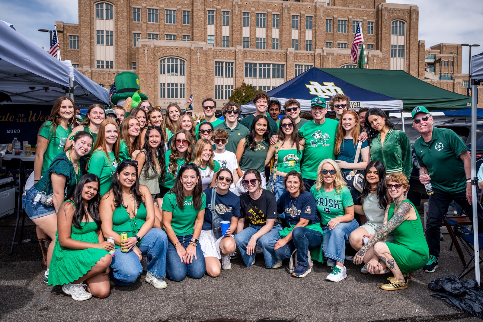 Large Notre Dame tailgate group in green gathered beneath tents outside the stadium.